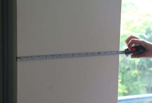 Mesure de la largeur d’un pan de mur à l’aide d’un mètre ruban.